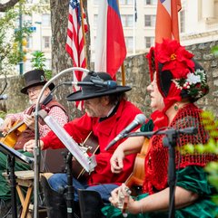Four living historians in 1830s attire seated on a stage playing instruments