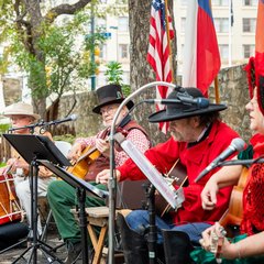 Four living historians in 1830s attire seated on a stage playing instruments