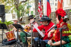 Four living historians in 1830s attire seated on a stage playing instruments