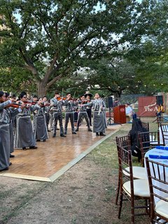 Mariachi performers playing instruments on a wooden dance floor in the gardens