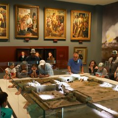 Visitors looking at a diorama of the Battle of the Alamo in a room with paintings on the wall
