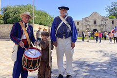 Boy in a David Crockett costume standing in between a living historian with a drum a another living historian in Alamo Plaza