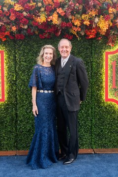 Woman in formal navy blue gown and man in a black tuxedo against a floral backdrop
