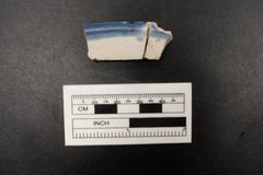 Fragment of ceramic with a blue border next to a ruler for size