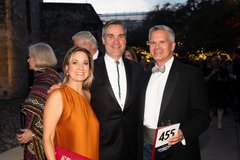 Woman in an orange sleeveless gown with two men, each wearing a black tuxedo