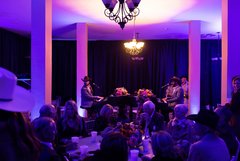 Table of seated guests in front of dueling pianos in Alamo Hall with purple uplighting