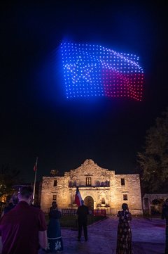 Texas flag in drone lights over Alamo Church at night