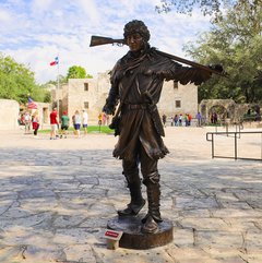 Bronze statue of David Crockett in Alamo Plaza with Alamo Church in the background