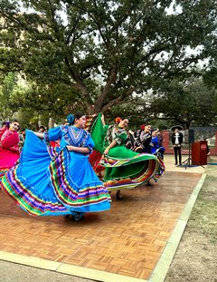 Ballet Folklorico dancers in bright pink, blue, and green dresses on a dance floor