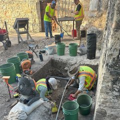 Two archaeologists working in an excavation unit surrounded by a perimeter of green buckets