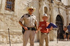 Alamo Ranger and a boy holding a folded Texas flag in front of Alamo Church