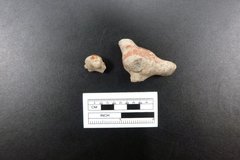 Two fragments of a ceramic figurine next to a ruler for size