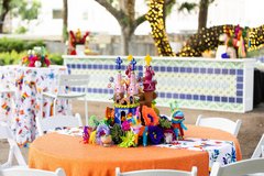 Painted steeple and colorful pinatas as a centerpiece on a table with orange linens and an otomi runner