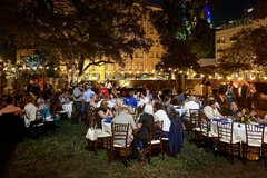 Guests seated in tables enjoying the event in Alamo Gardens, illuminated by string lights