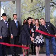 A woman holding a knife after cutting through a red ribbon in front of a building in a line with other people