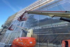 Crane installing scrim cover over scaffolding on a building