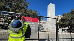 Construction worker affixing sign to fencing around Alamo Cenotaph