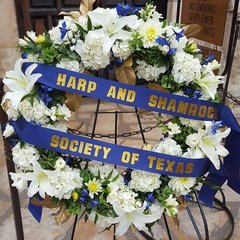 Wreath with white flowers and a blue ribbon with the words Harp and Shamrock Society of Texas