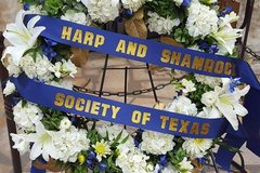 Wreath with white flowers and a blue ribbon with the words Harp and Shamrock Society of Texas