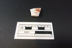 Single Chinese porcelain fragment next to a ruler to show size