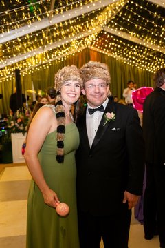 Man and woman in black tie attire both wearing coonskin caps under string lighting of dance floor