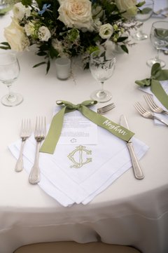 Table setting with white linen napkin with a green C monogram and green ribbon