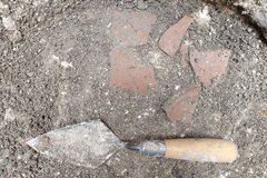 Red clay deposits at bottom of excavation unit next to a shovel