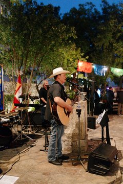 Man wearing a cowboy hat and playing the guitar on a stone platform outdoors