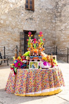 Round table with colorful ribbons and painted mission centerpiece with open guest book outside of Alamo Church