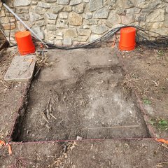 Two orange buckets next to a stone wall by a square excavation unit