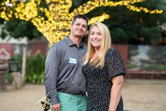 Man and woman smiling in front a tree wrapped with white lights in branches