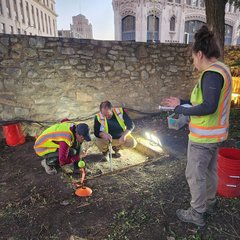 Archaeologists taking measurements at night in a lighted excavation unit