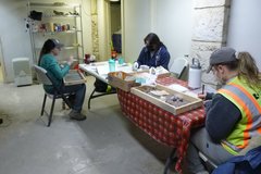 Three people sitting around a long table examining artifacts