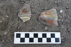 Two pieces of ceramics with bright orange markings next a ruler on a bed of gravel