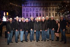 Group of auctioneers wearing black jackets and cowboy hats in a row in front of Alamo Church