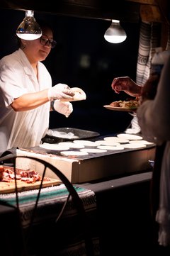 Server preparing gorditas on a grill, handing one to a guest