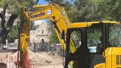 Yellow construction vehicle doing work in the dirt with Alamo Church in the background