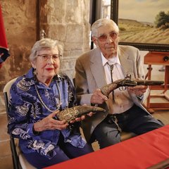 Louise and Donald Yena seated at a table with a red tablecloth holding artifacts