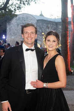 Couple with male in a black tuxedo and woman in a black formal gown smiling at an outdoor event