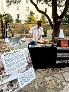 Man slicing steak on a cutting board next to a poster that describes Chuckwagon Cooking