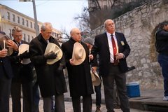Men standing in a line with hats lowered to honor Alamo Defenders
