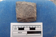 Square gunflint on a blue background next to a ruler for size