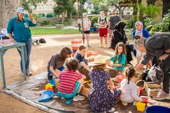 Group of children sitting around a small sandbox digging for dirt in a mock excavation