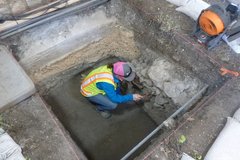 Archaeologist cleaning inside of excavation unit with a brush