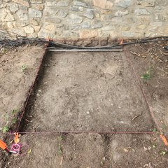 Dirt in square excavation unit next to a stone wall