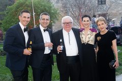 Three men in black tuxedos with two women in formal gowns in an garden
