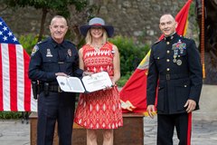 Wife of Marine General and an Officer holding a certificate in front of the American and Marine flags