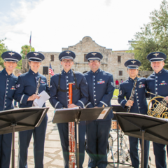 Six Air Force musician in blue uniform in front of Alamo Church holding instruments