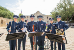 Six Air Force musician in blue uniform in front of Alamo Church holding instruments