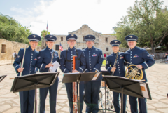 Six Air Force musician in blue uniform in front of Alamo Church holding instruments